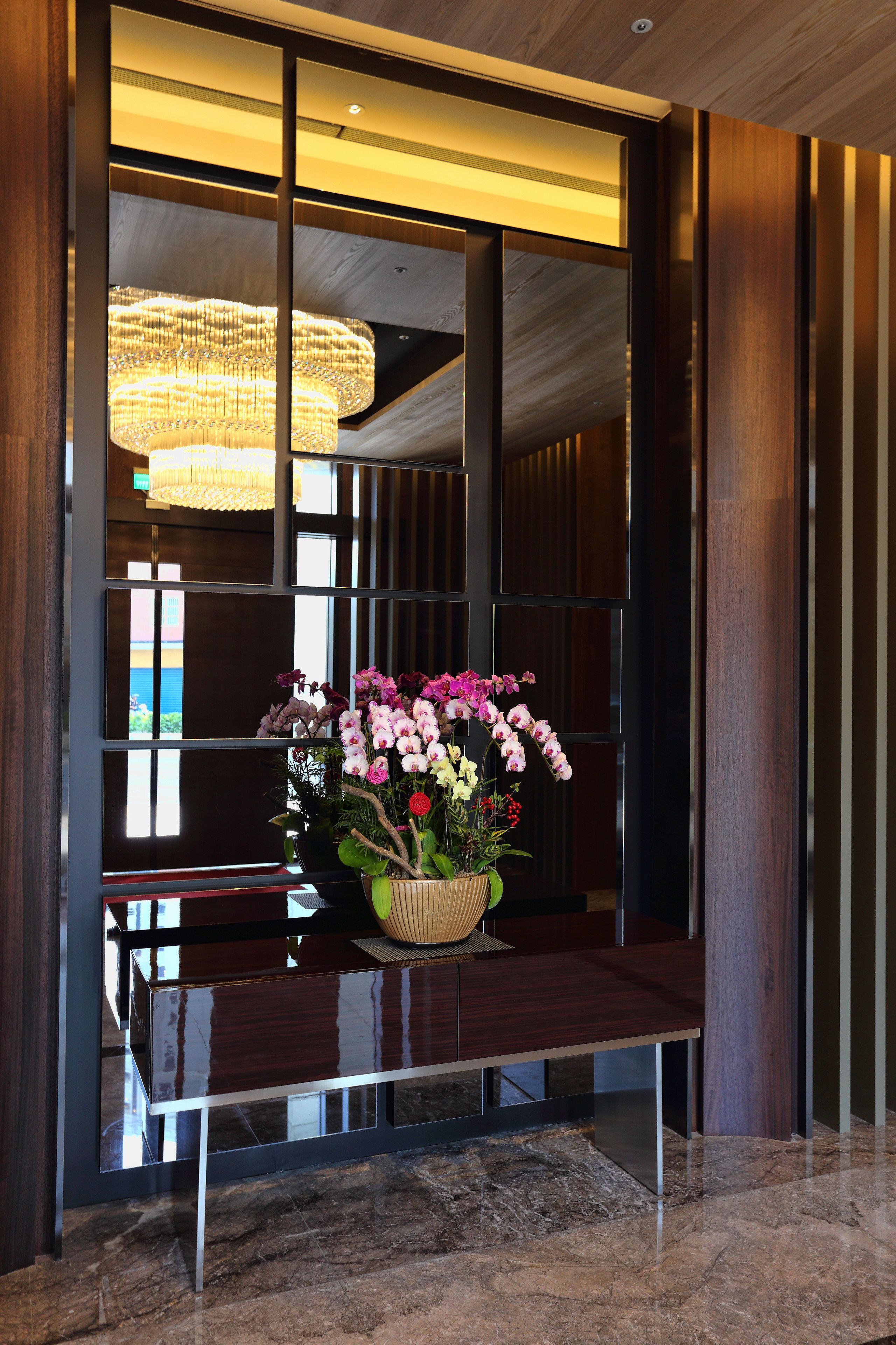 A reception area with a wooden reception desk, a large vase of flowers, and a modern chandelier.