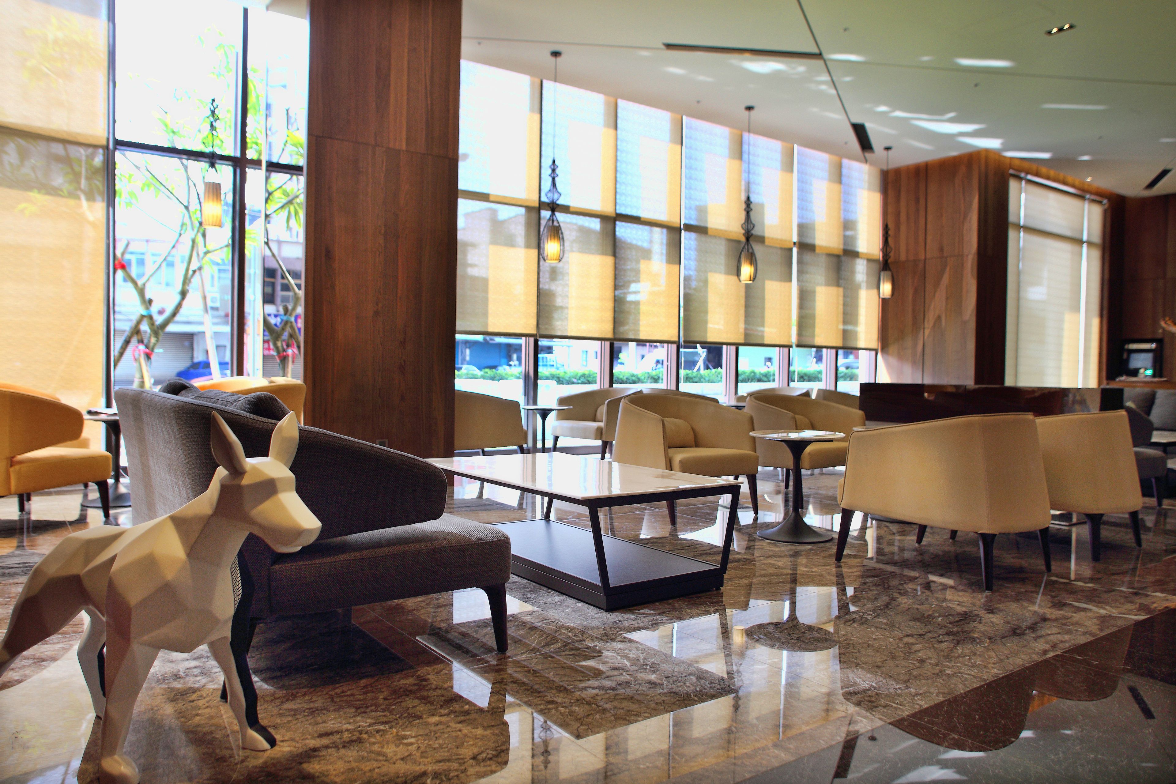 A modern lobby with a polished marble floor, contemporary furniture, and large windows offering a view of the outdoors.