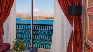 A room with a view of a lake, a red velvet sofa, and a vase with flowers. - Hotel Chems du Lac (Bine el Ouidane)