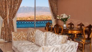 A room with a sofa, a table with a vase of flowers, and a view of mountains and a body of water. - Hotel Chems du Lac (Bine el Ouidane)
