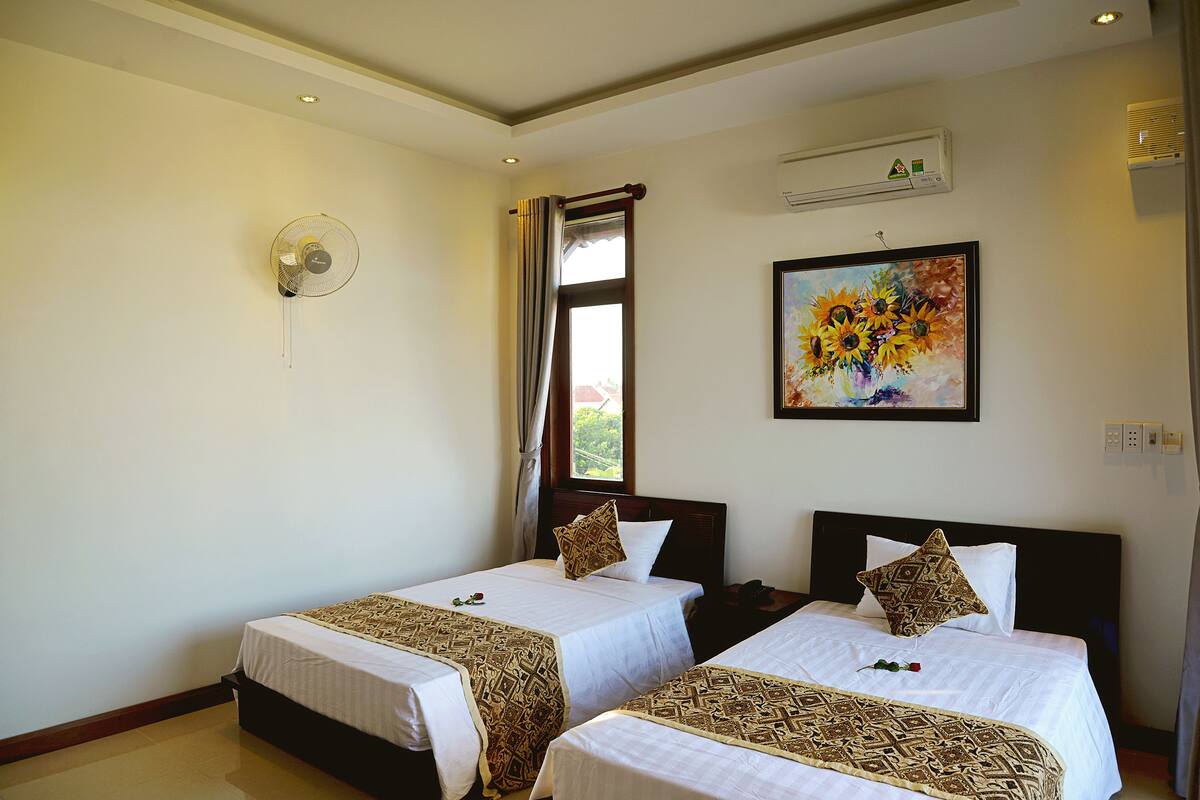 Ein Hotelzimmer mit zwei Betten, einem Deckenventilator, einer Klimaanlage und einem fenster mit Vorhängen.