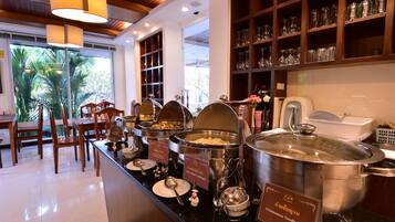 A buffet area with various food stations, including a large pot of Vietnamese noodle soup, and a seating area with tables and chairs.