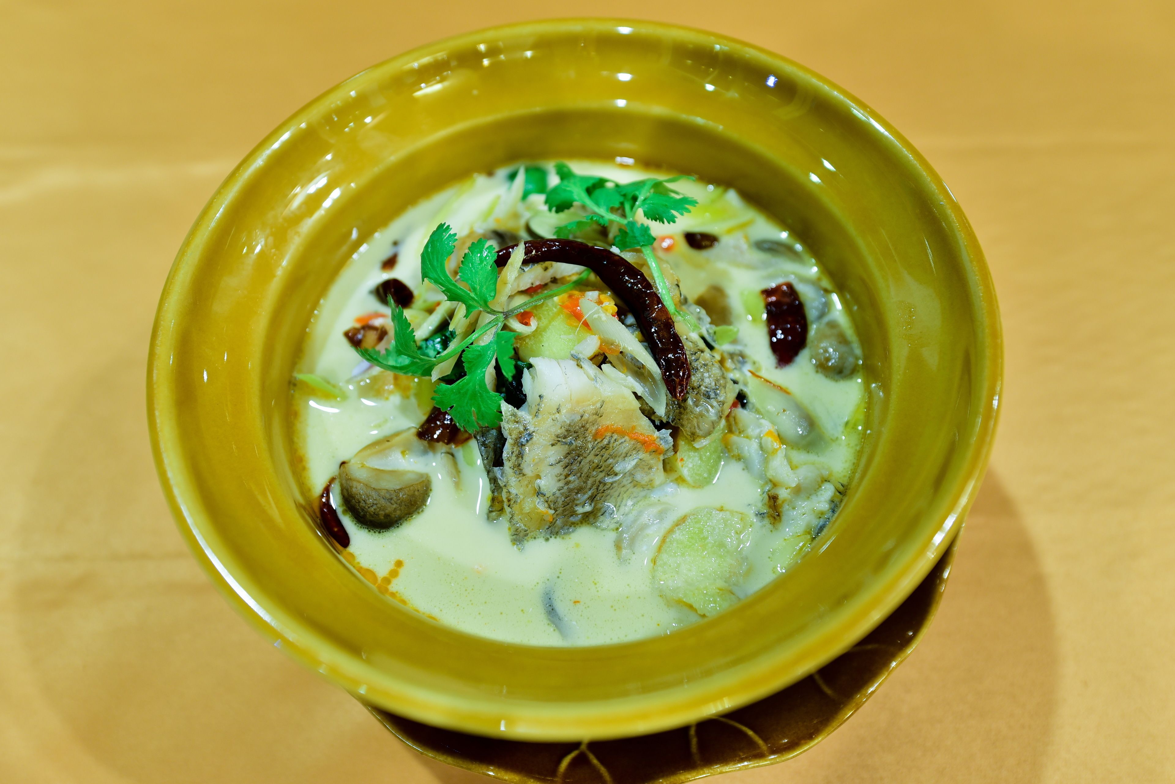 A bowl of soup with various ingredients, including fish, vegetables, and herbs, served in a yellow bowl.