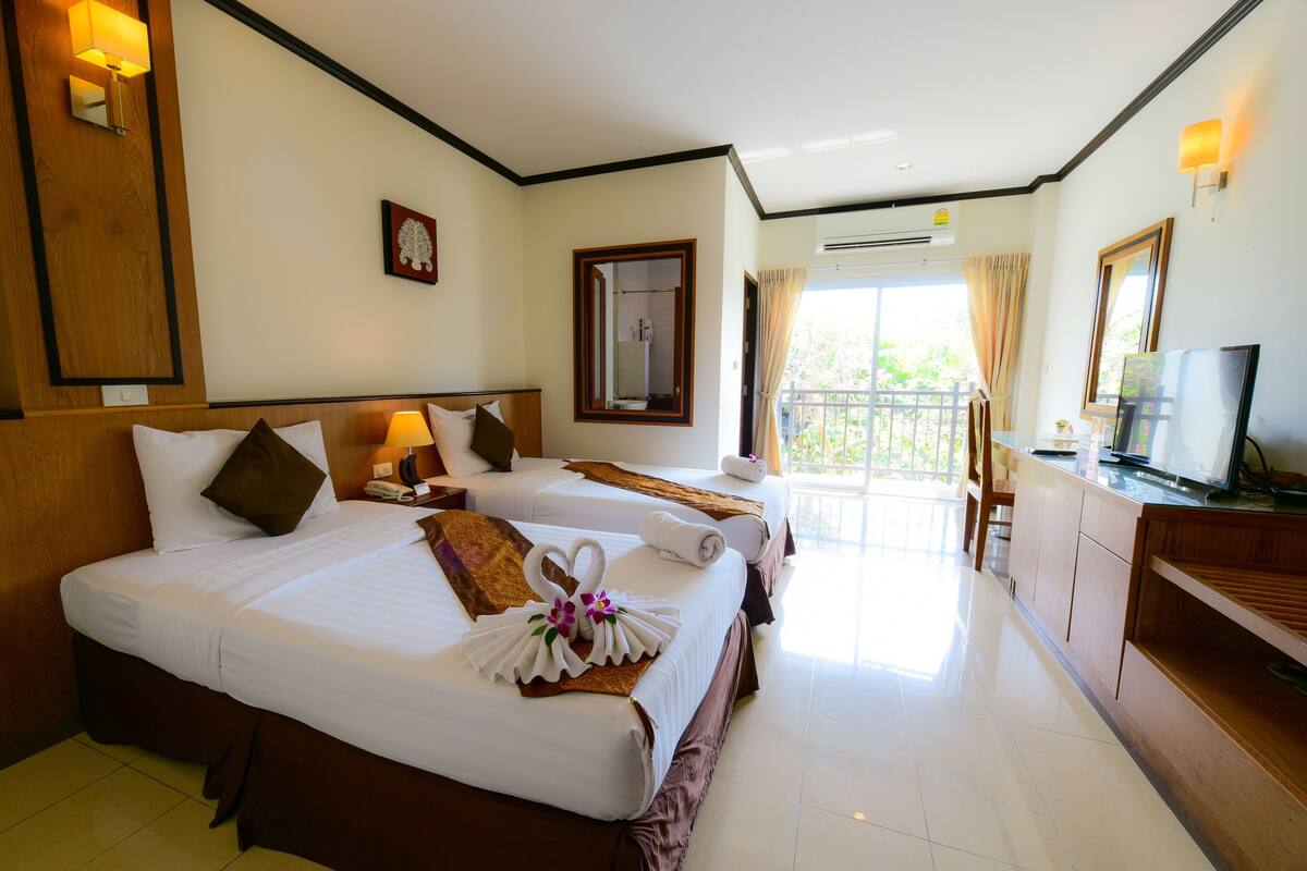A hotel room with two beds, a TV, a desk, and a balcony with a view.