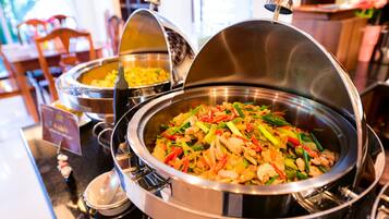 A buffet with various dishes, including a stir-fry with vegetables and meat, covered in metal serving dishes.