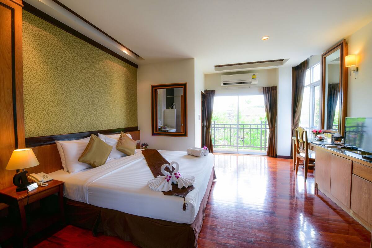 A hotel room with a large bed, a desk with a lamp, a mirror, and a view of the outdoors.