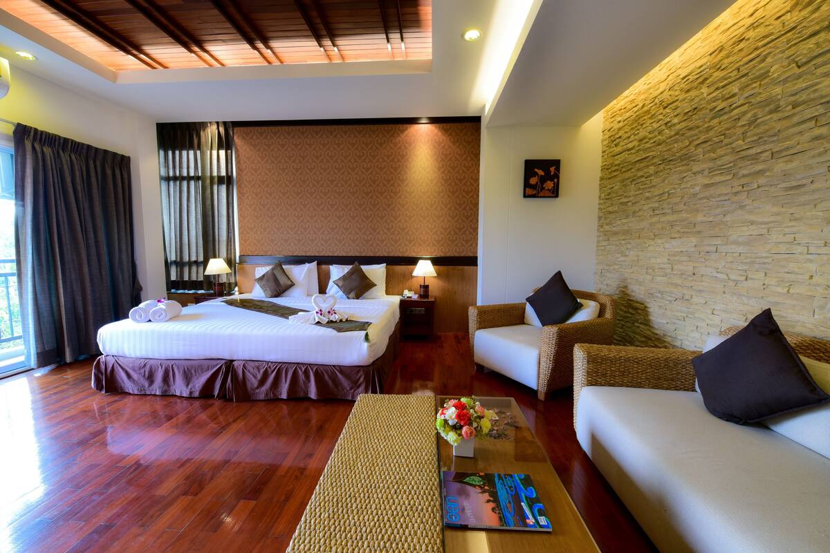 A hotel room with a large bed, a sofa, a coffee table, and a stone wall.