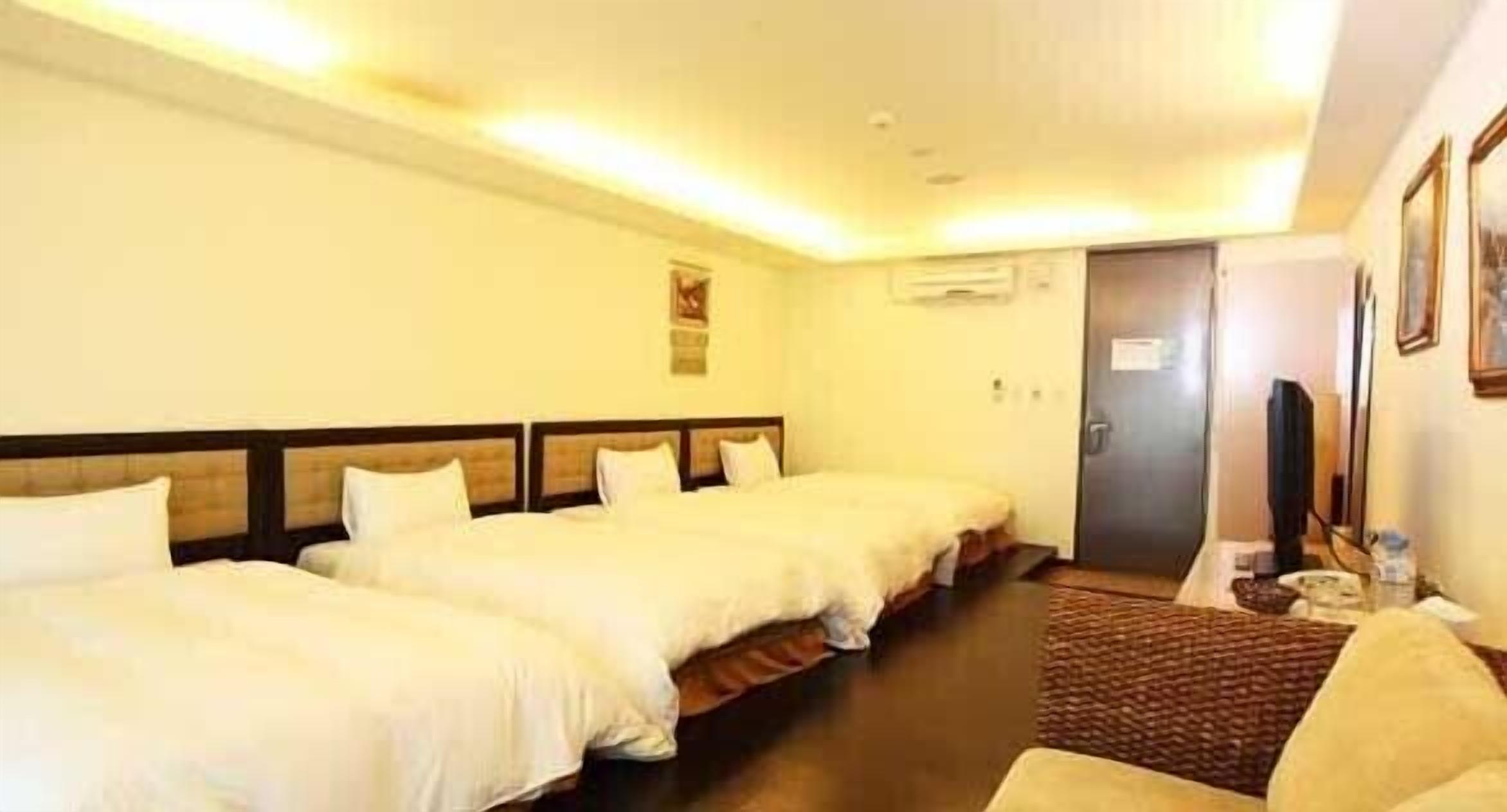 A hotel room with three single beds, a small desk with a chair, and a television.