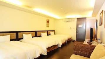 A hotel room with three single beds, a small desk with a chair, and a television.