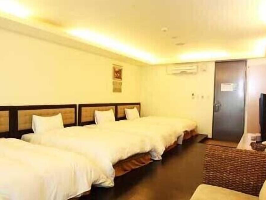 A hotel room with three single beds, a small desk with a chair, and a television.