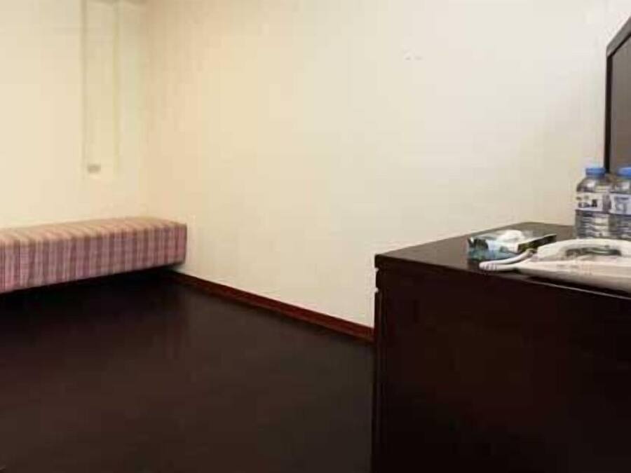 Une chambre d’hôtel avec un plancher en bois foncé, un petit banc rose et un bureau en bois foncé sur lequel se trouvent un téléphone et une bouteille d’eau.