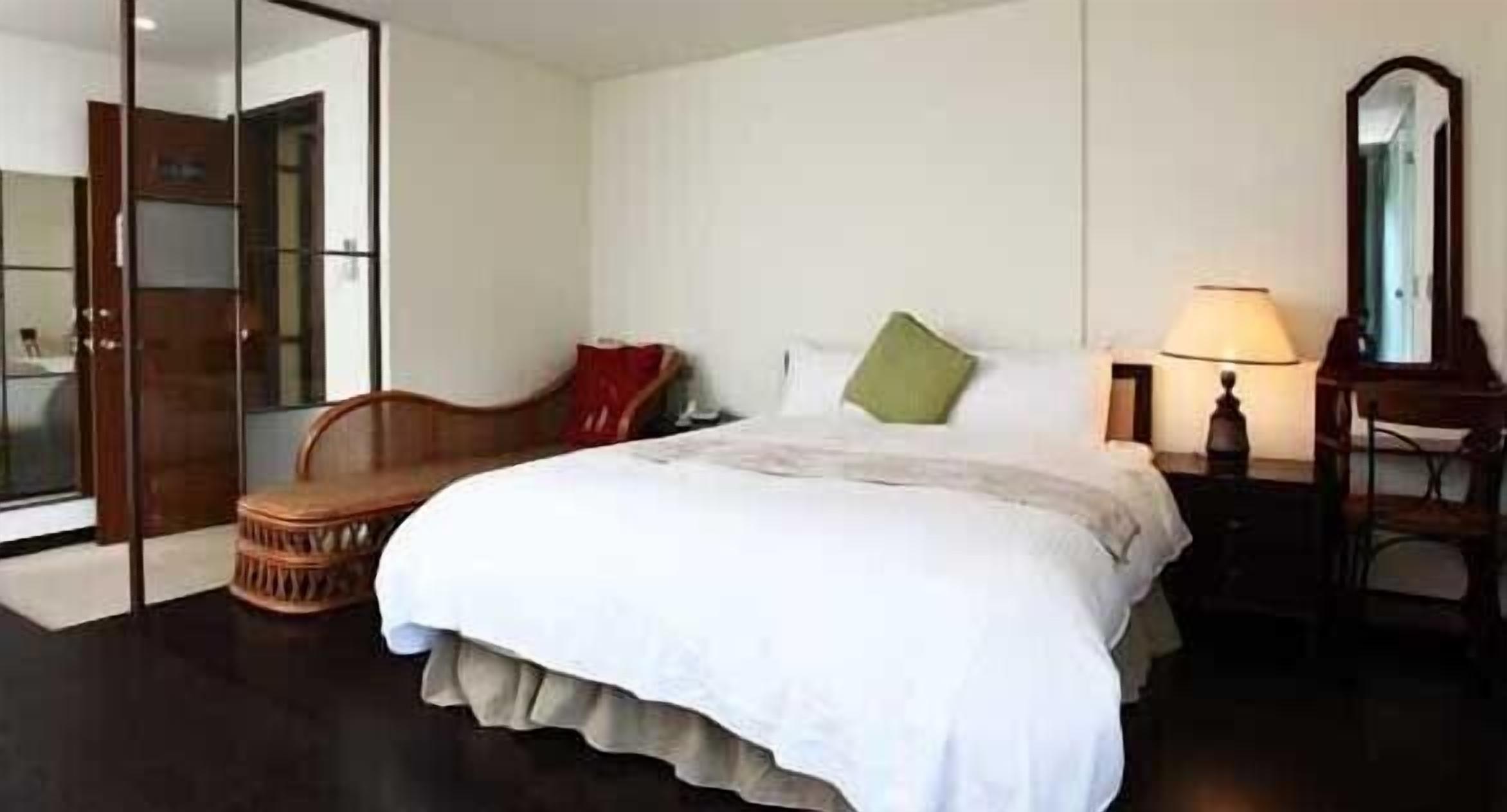 A hotel room with a bed, a chair, a lamp, and a mirror.