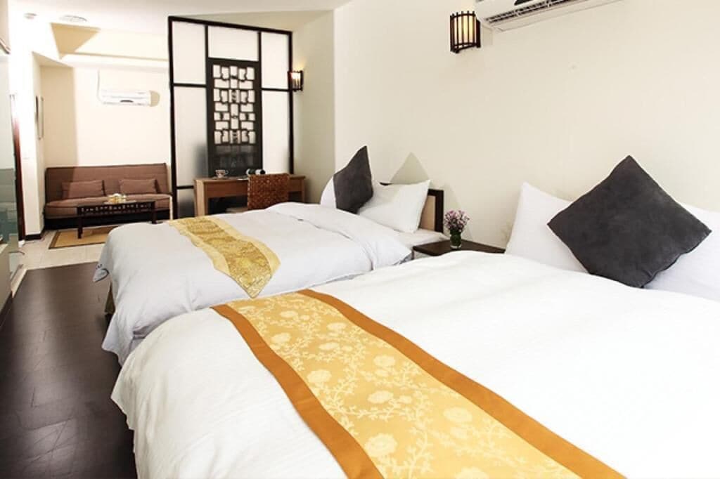 Habitación de hotel con dos camas, un sofá, una mesita y un biombo decorativo.