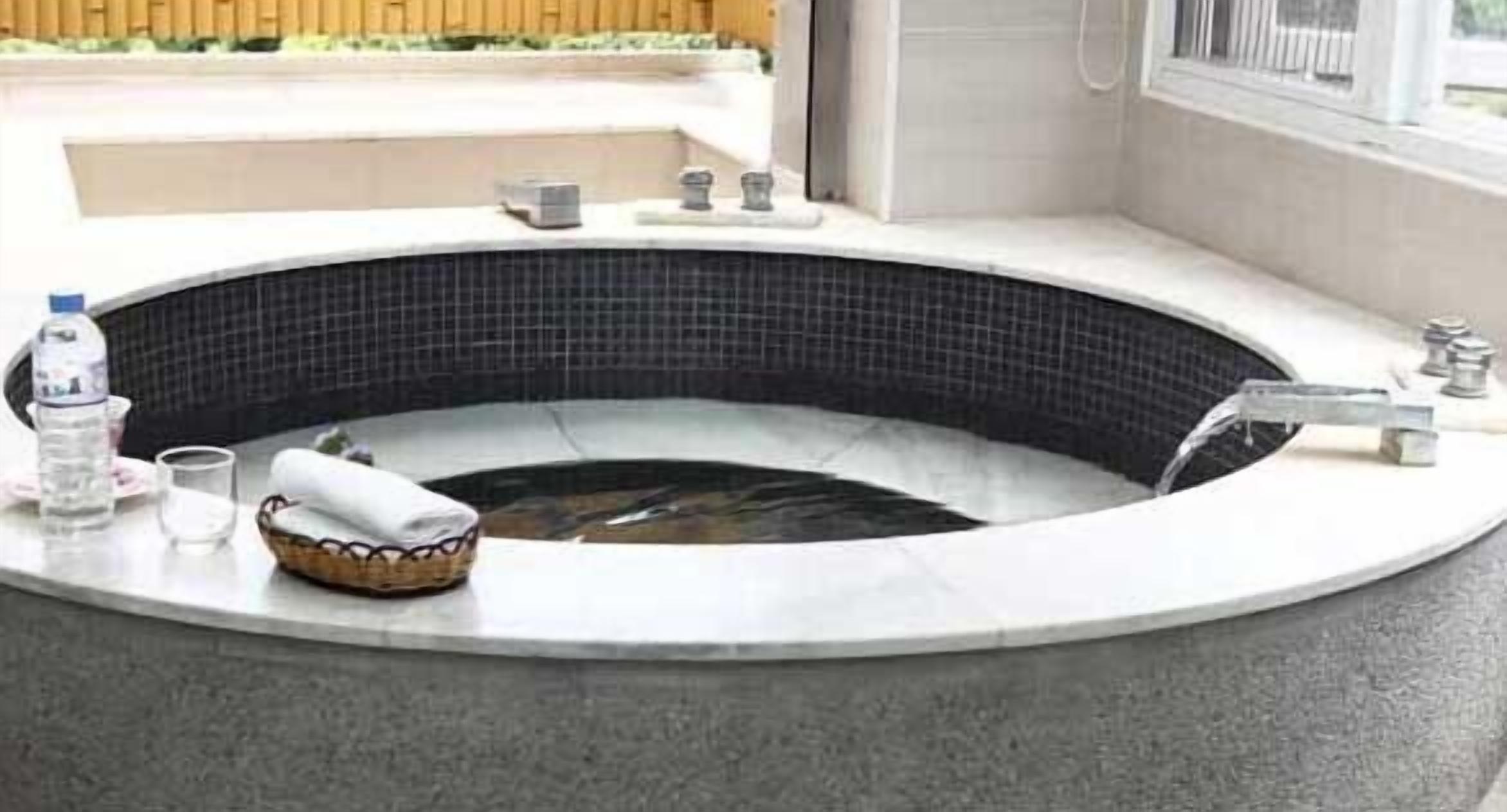 Una bañera de hidromasaje con interior de azulejos negros, una cesta pequeña y una toalla.