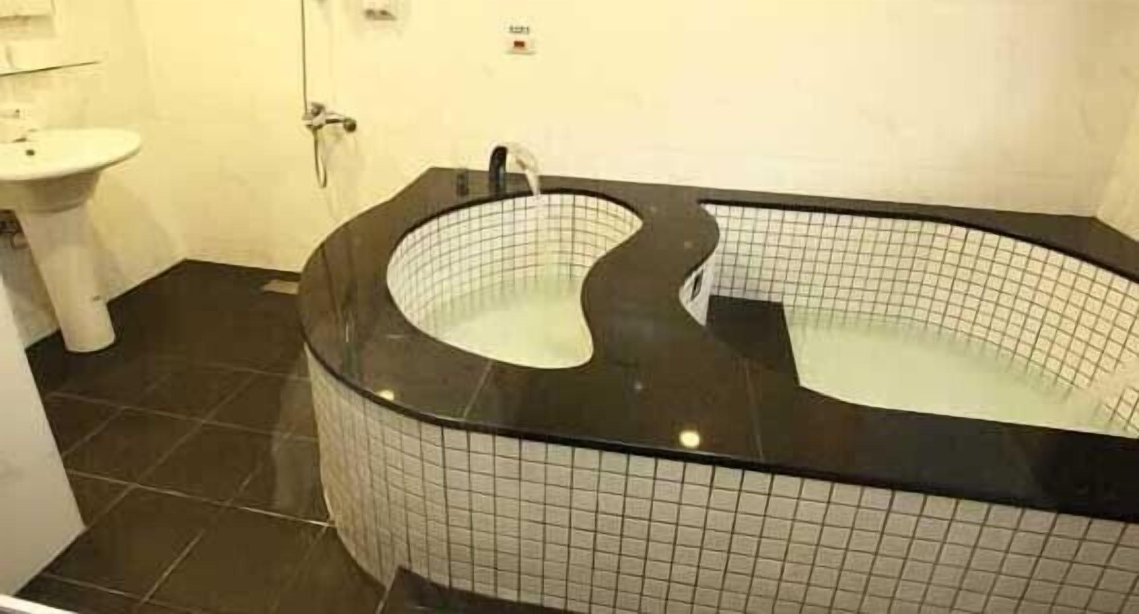 Une salle de bain avec une baignoire noire, un lavabo blanc et un sol carrelé.