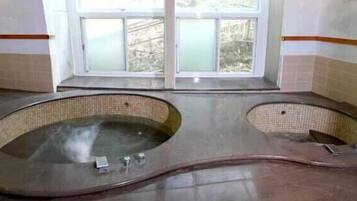Una habitación con dos tinas de hidromasaje grandes y ovaladas, con interiores revestidos de azulejos, situadas bajo un ventanal con vidrios esmerilados.