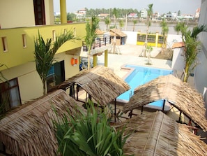 A pool area with thatched umbrellas, a view of the surrounding buildings, and a clear sky. - Oasis Hotel (An Hoi)