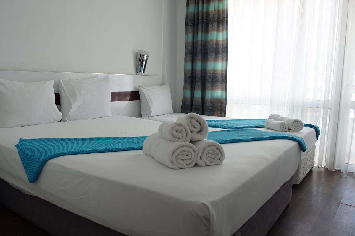 A hotel room with two beds, white bedding, and rolled towels.