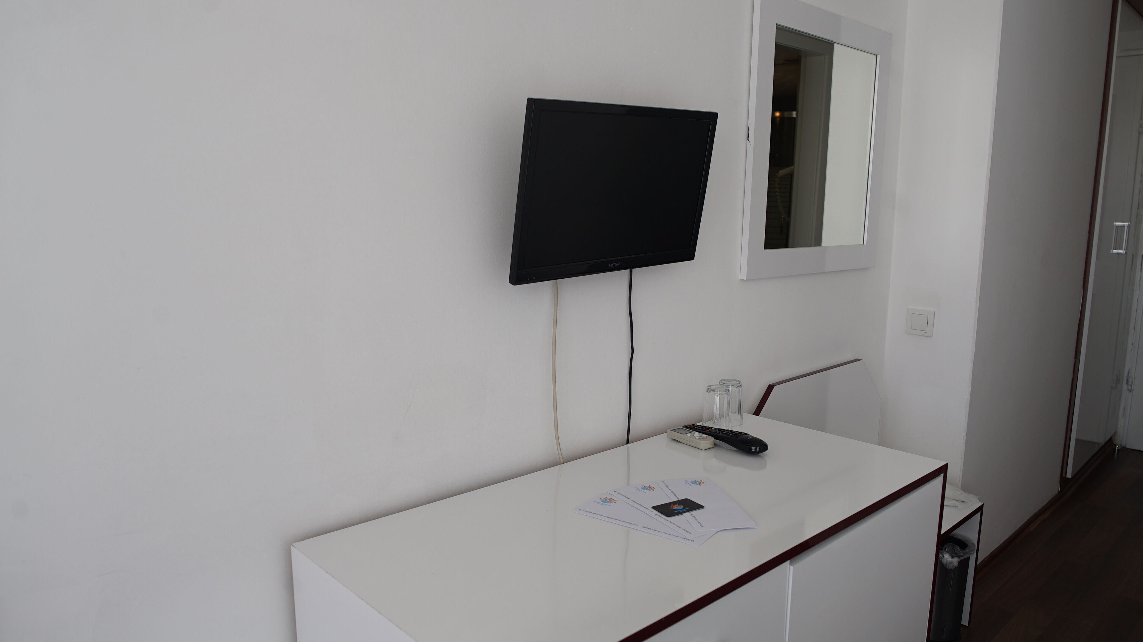 Eine weiße Wand mit einem montierten Fernseher und einem Spiegel über einer weißen Arbeitsplatte.