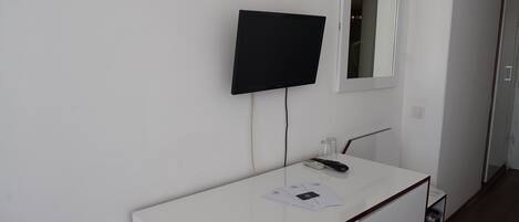 Eine weiße Wand mit einem montierten Fernseher und einem Spiegel über einer weißen Arbeitsplatte.