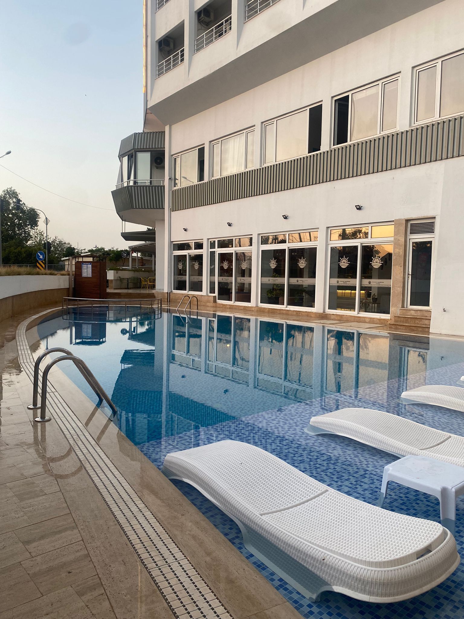 A swimming pool with lounge chairs, a covered seating area, and a building with multiple windows and balconies.