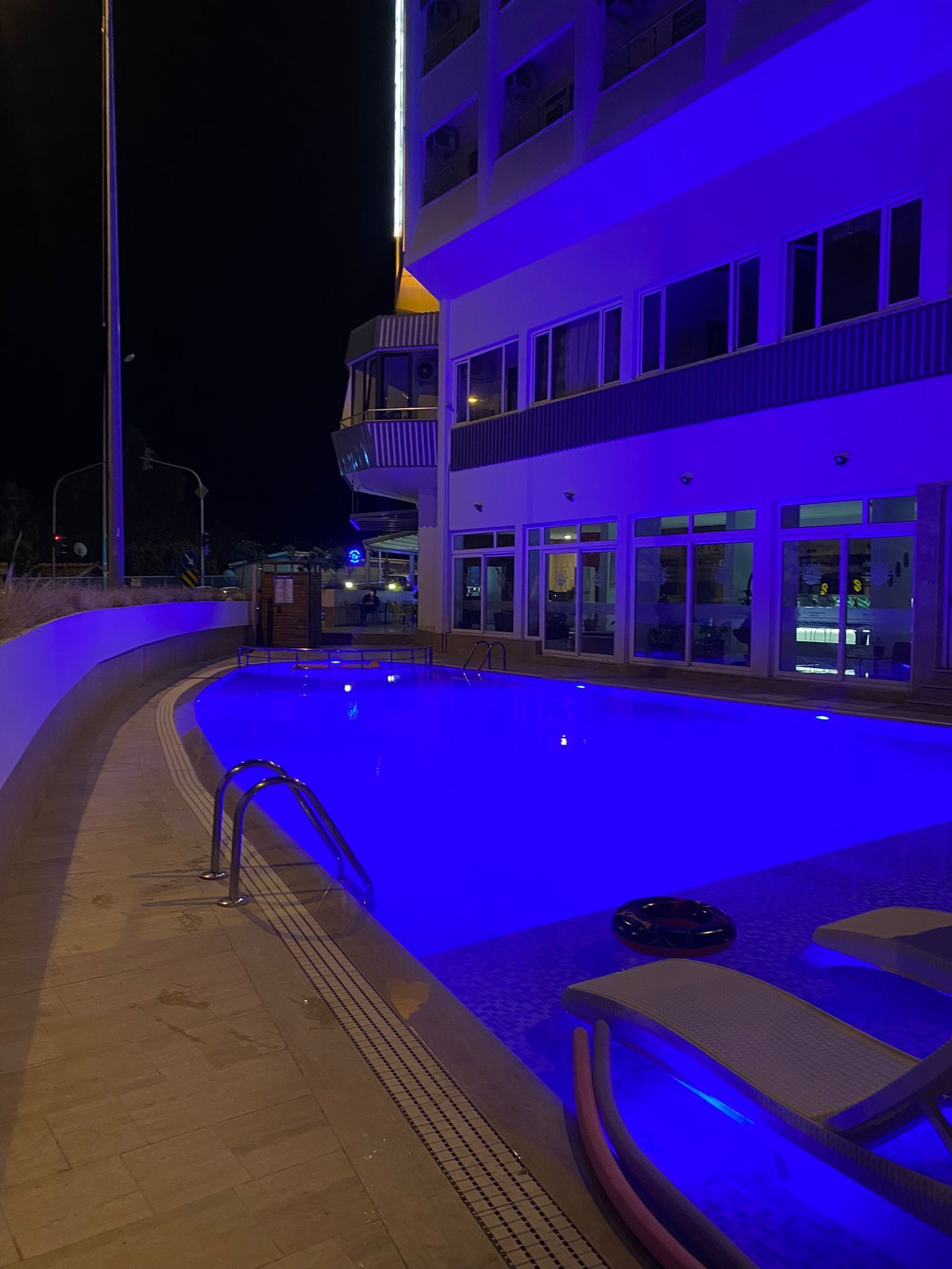 A swimming pool with a blue-lit edge, surrounded by a building with multiple balconies and windows.
