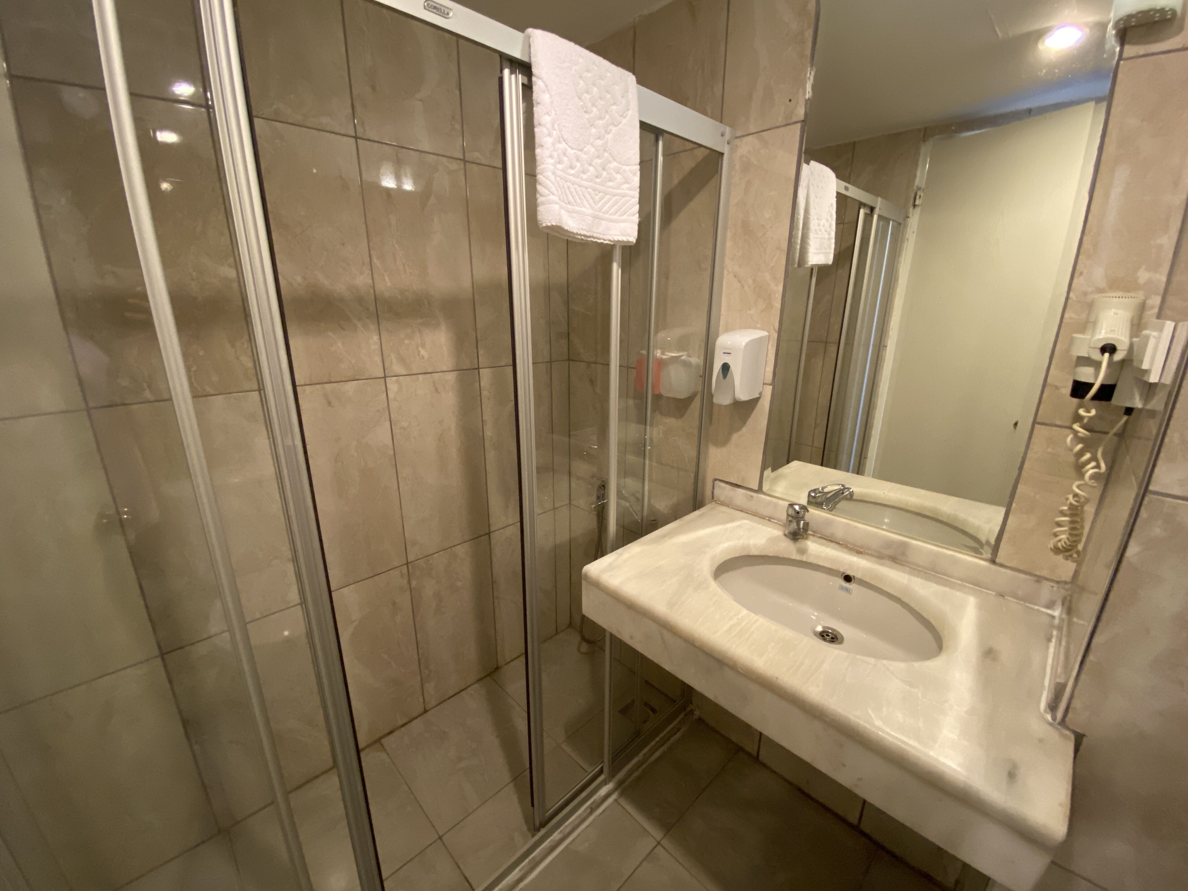 A modern bathroom with a glass shower enclosure, a sink with a mirror, and a hand soap dispenser.