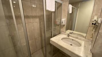 Een moderne badkamer met een douchecabine van glas, een wastafel met spiegel en een handzeepdispenser.