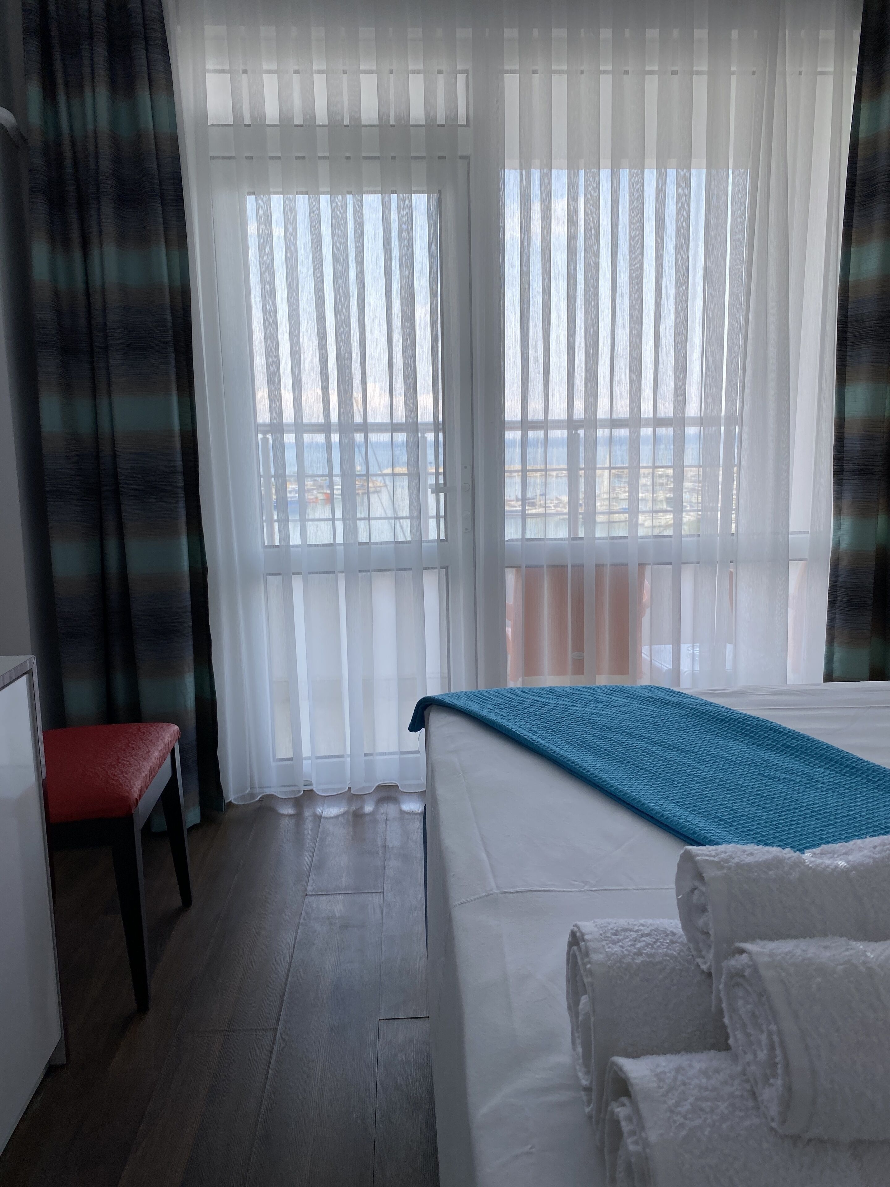 A hotel room with a bed, a bench, and a view of the sea through large windows.