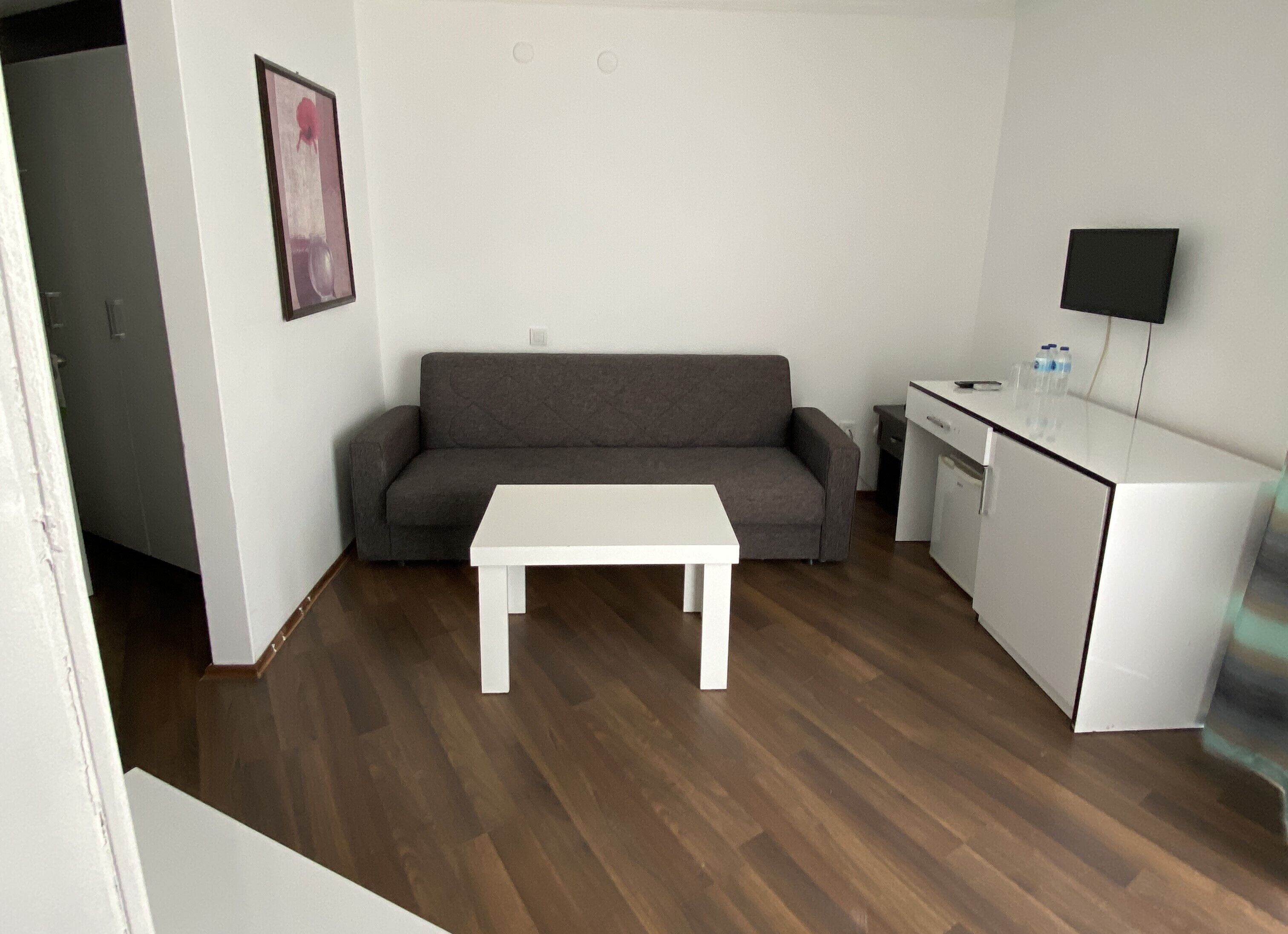 A compact living space with a grey sofa, a white table, and a small kitchenette.