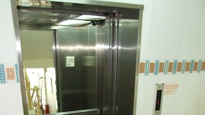 Een lift met een metalen afwerking, een bedieningspaneel en een geruit vloertje.