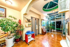 Welcome to our hotel lobby, featuring a spacious layout with a large potted plant, a desk, and a glass door leading outside.