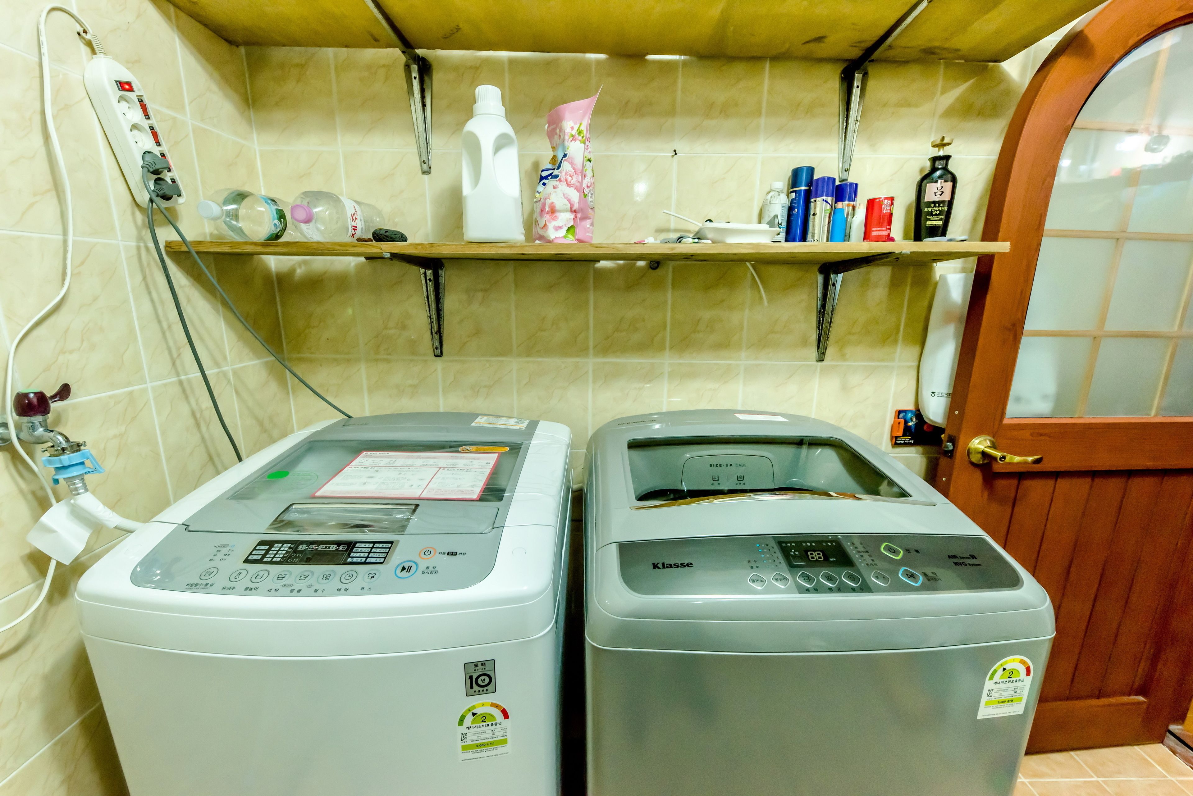 Deux machines à laver à chargement frontal se trouvent dans une buanderie, avec une étagère au-dessus contenant divers flacons et récipients.