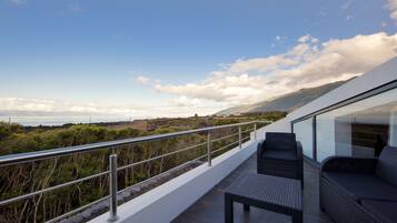 Un balcón con vista al mar y a las montañas, amueblado con un sofá y una mesa.