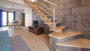 Un salon moderne avec un escalier en bois, un coin repas et un mur en pierre.