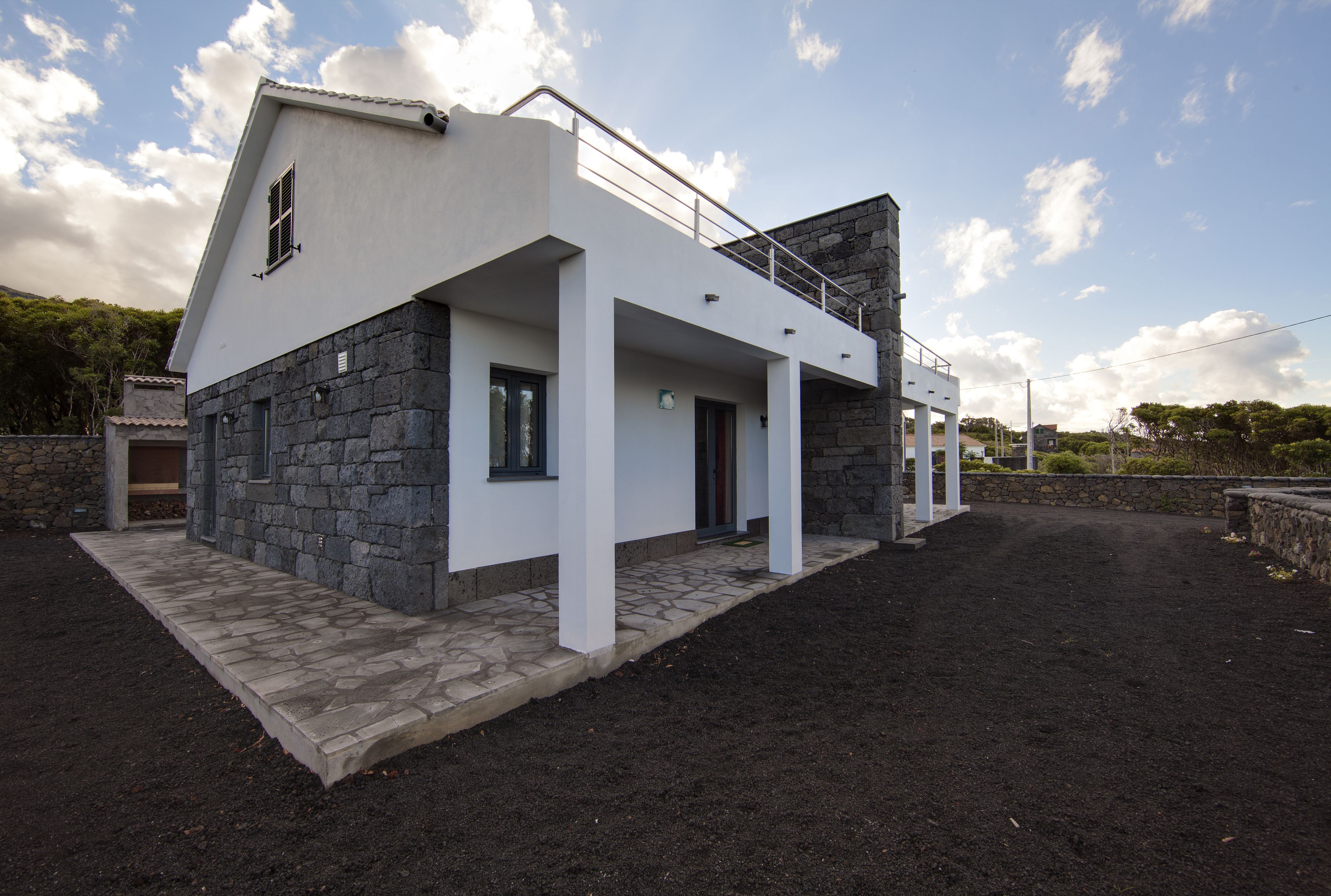 Una casa moderna con fachada de piedra, un balcón y un camino de entrada pavimentado.