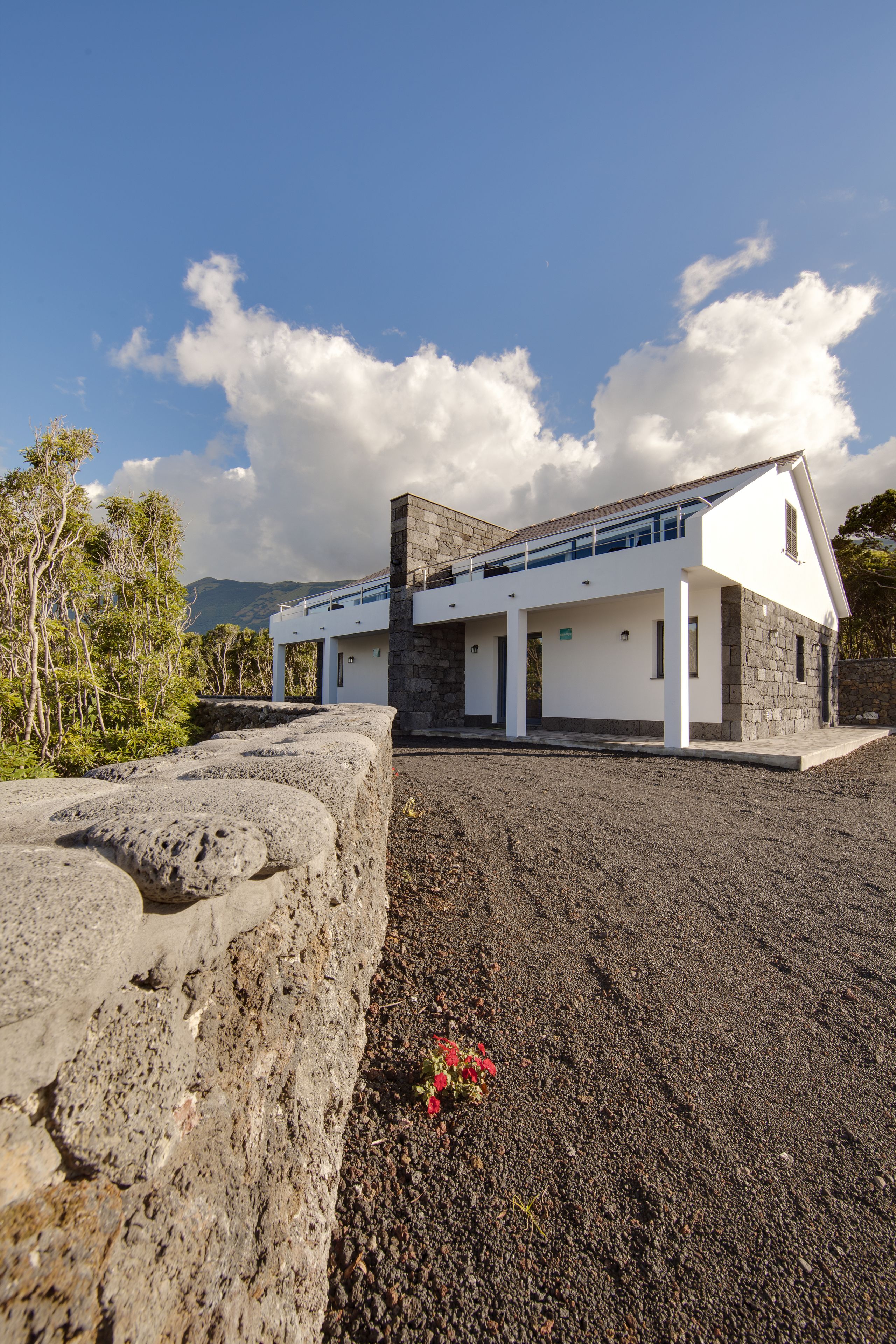 Una casa moderna con fachada de piedra, techo plano y un balcón con vistas a un paisaje rocoso.