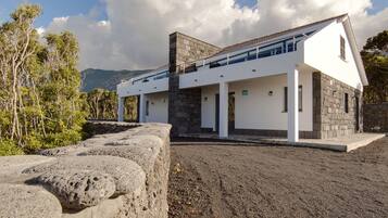 Una casa moderna con fachada de piedra, techo plano y un balcón con vistas a un paisaje rocoso.