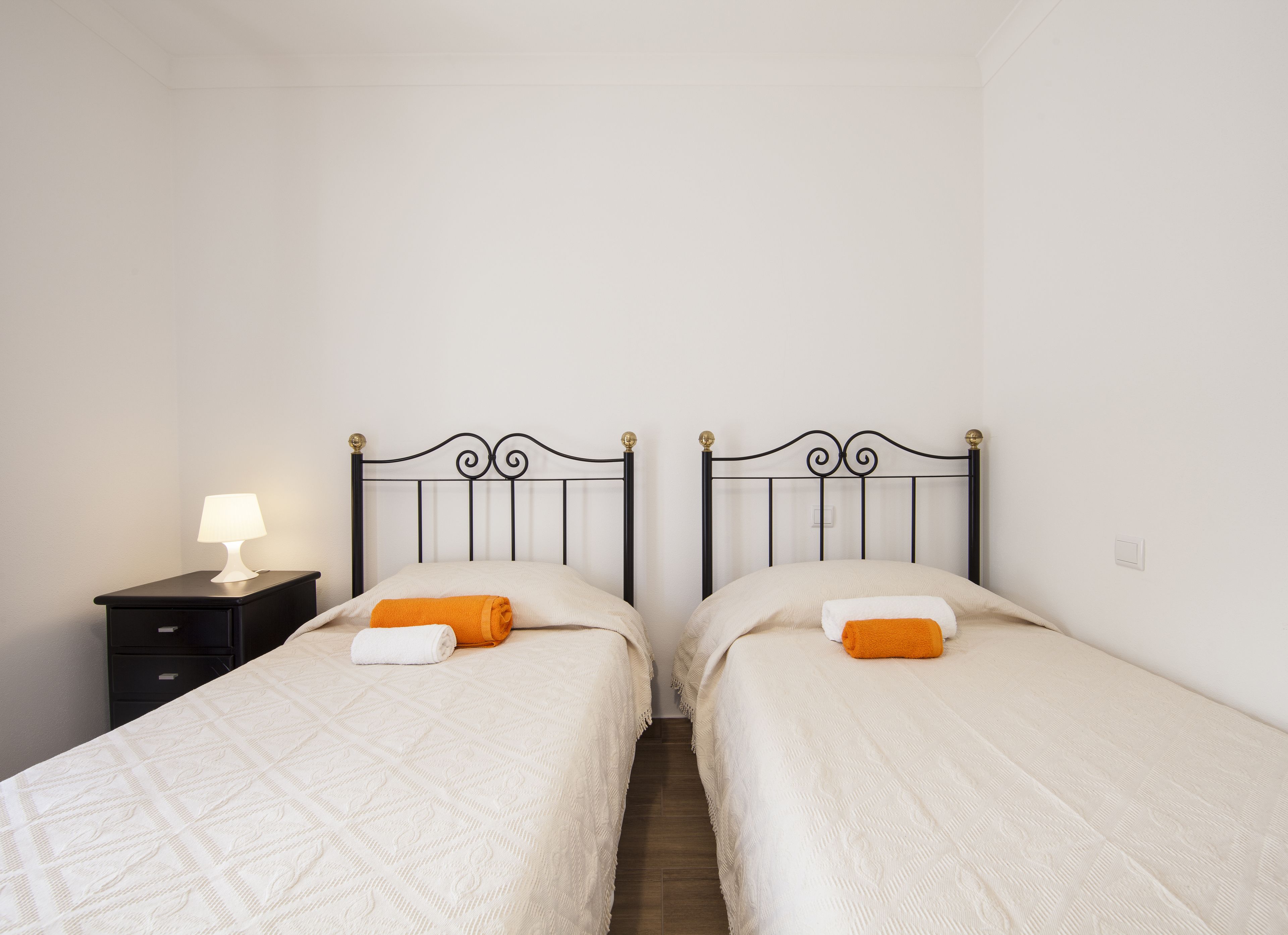 Una habitación con dos camas, cada una con cabecera y mesita de noche con lámpara.