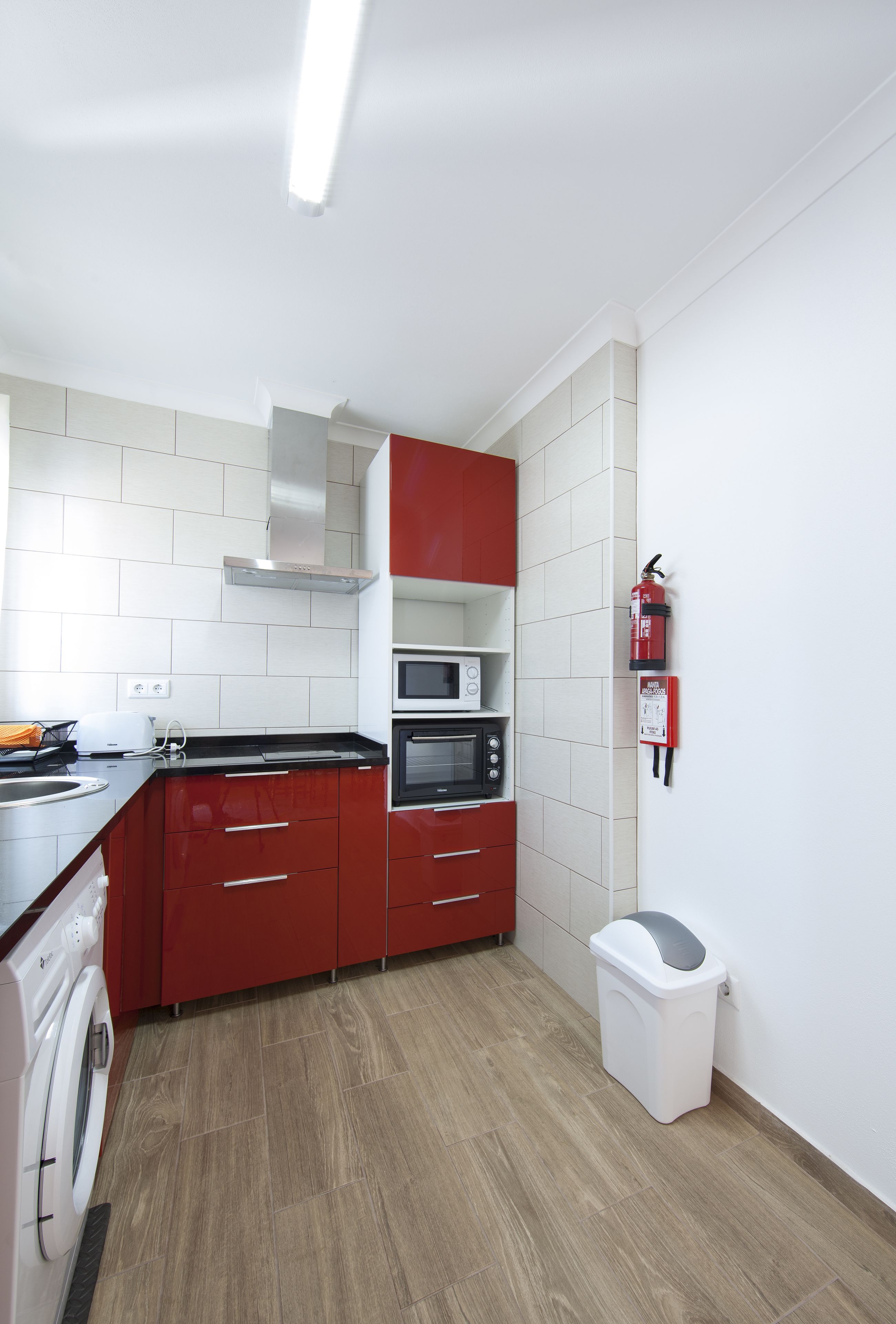 A compact kitchen with red cabinets, a microwave, a stove, and a trash bin.
