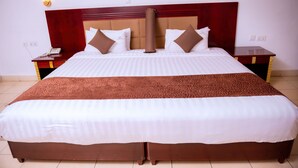 A large bed with a wooden headboard, two bedside tables, and wall-mounted light fixtures. - Quiet Haven Hotel (Kigali)