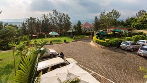 A spacious parking area with a paved surface, surrounded by lush greenery and a view of distant hills. - Quiet Haven Hotel (Kigali)
