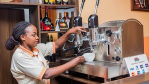 A barista preparing a coffee at a commercial espresso machine. - Quiet Haven Hotel (Kigali)