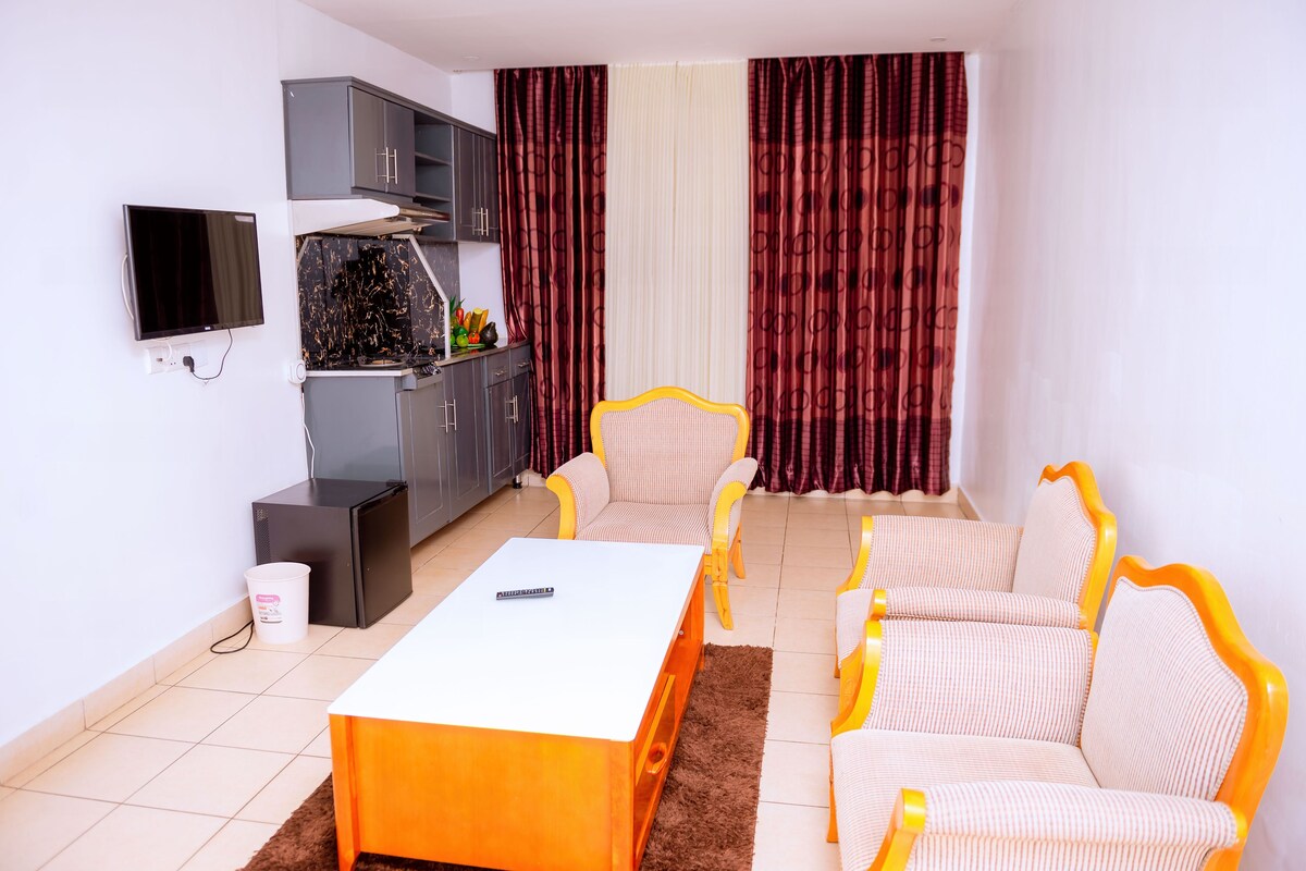 Un espacio habitable compacto con sofá, mesa de centro, televisor, kitchenette y cortinas.