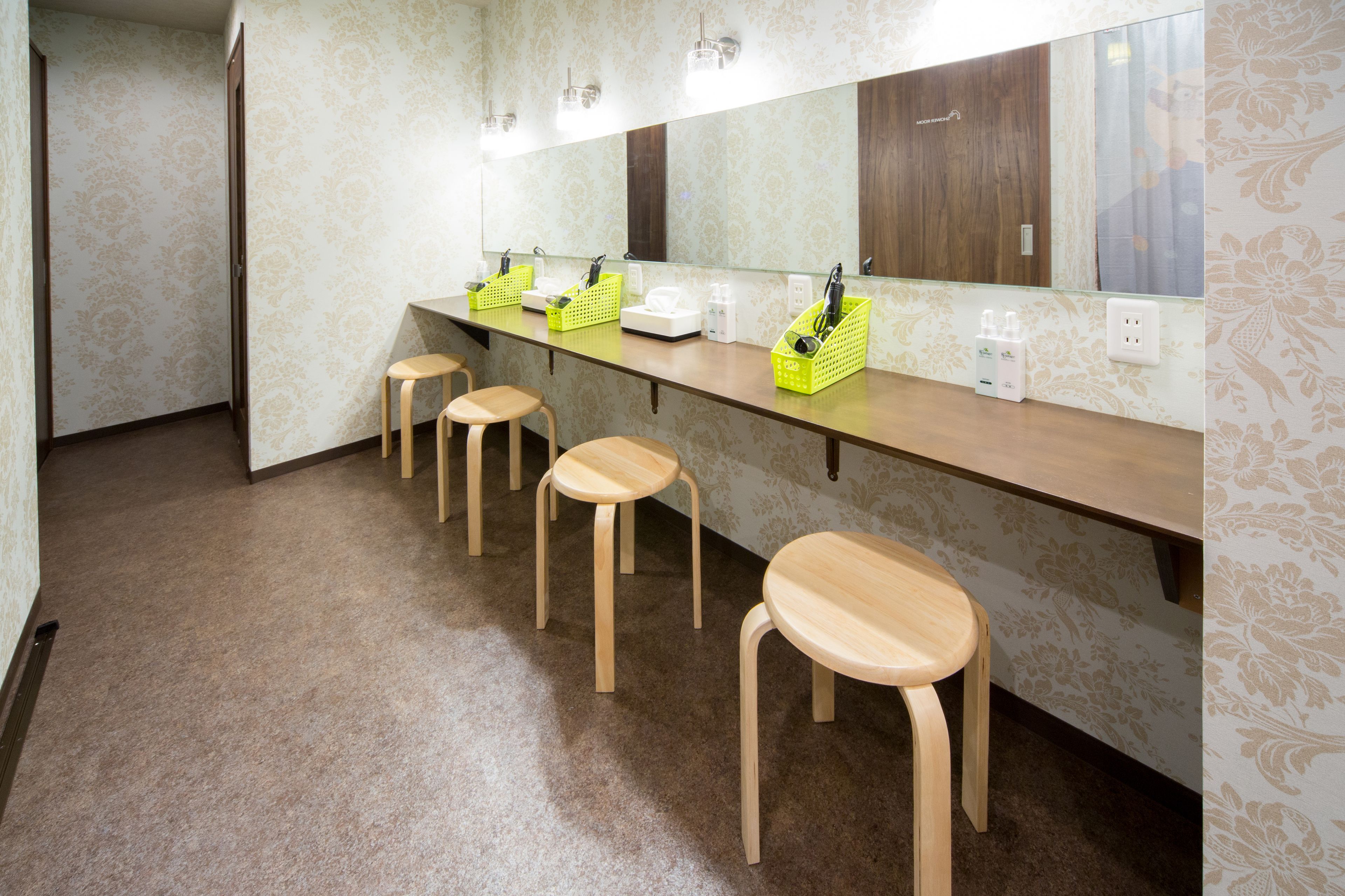 A bathroom with a long counter, four wooden stools, a mirror, and a patterned wall.