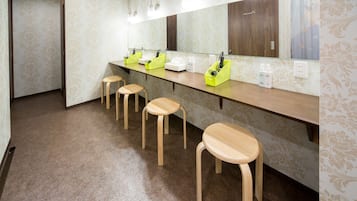 A bathroom with a long counter, four wooden stools, a mirror, and a patterned wall.