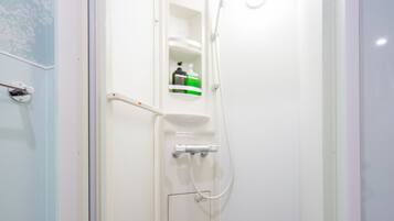 A small, enclosed shower stall with a white door, a shelf with toiletries, and a showerhead.