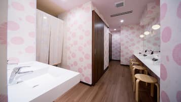 Baño con un lavamanos grande, taburetes de madera, un espejo y papel tapiz con estampado floral rosa.