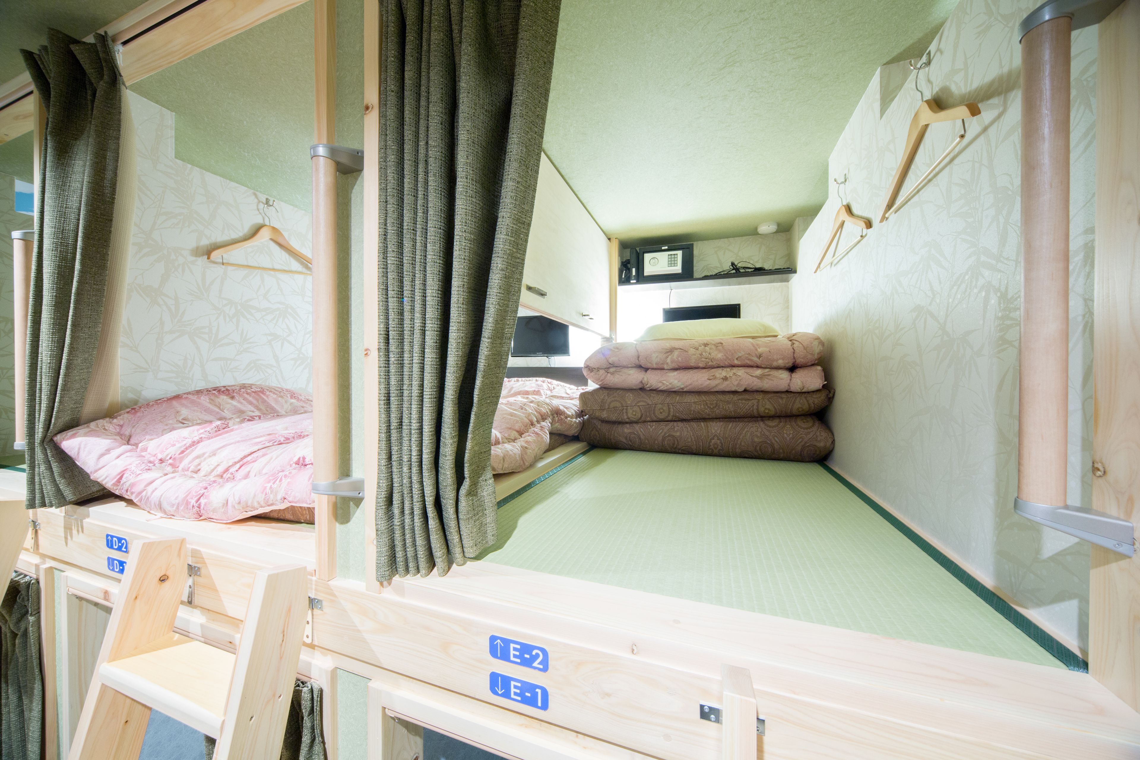 A bunk bed with a green mattress, a wooden headboard, and a small shelf. There is a wooden hanger on the wall and a window with curtains.
