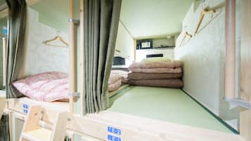 A bunk bed with a green mattress, a wooden headboard, and a small shelf. There is a wooden hanger on the wall and a window with curtains.